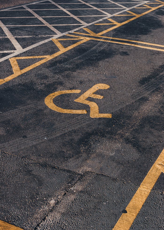 Overhead view of an accessible parking symbol on asphalt with yellow lines.